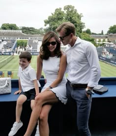 a man and woman are sitting on a bench at a tennis match with their son