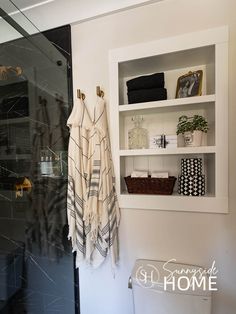 Recessed shelves in the bathroom which hold extra towels, bubble bath, basket with toilet paper, black and white containers which hold extra soap and cotton balls.