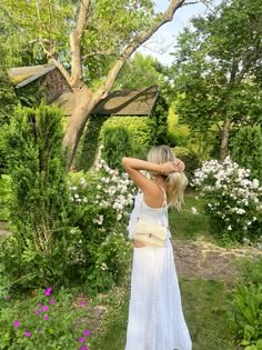 a woman in a white dress is walking through the grass and bushes with her back to the camera