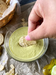 a person dipping some food into a small glass bowl with crackers on the side