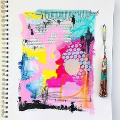 an art journal with colorful abstract paintings and a brush next to it on a white surface