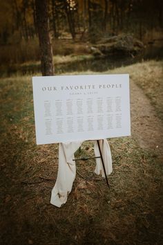 a white sign sitting on top of a grass covered field next to a forest filled with trees