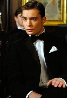 a young man in a tuxedo sitting at a table with other men behind him