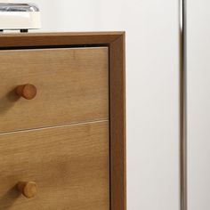 a wooden dresser with two drawers next to a white wall and a metal object on top