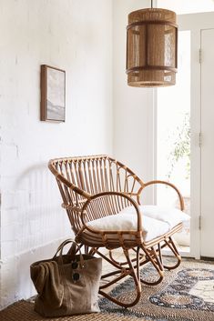 a wicker rocking chair next to a white brick wall with a handbag on the floor