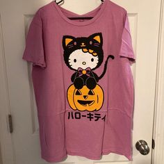 Hello Kitty Pumpkin T-Shirt Get Ready For Halloween Every Day With The Purr-Fect Tee! This Tee Features Hello Kitty Donning A Black Cat Costume And Sitting Atop A Jack-O'-Lantern. 100% Cotton Wash Cold; Dry Low Imported Pink Halloween Graphic Tee, Halloween Character Print Pink Top, Pink Character Print Tops For Loungewear, Cute Pink Hello Kitty T-shirt, Halloween Pink Cartoon Print Top, Pink Cat Print Graphic Tee, Pink Graphic Tee With Cat Print, Pink Cartoon Print Top For Halloween, Pink Halloween Cartoon Print Top