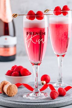 two glasses filled with raspberry wine next to a bowl of raspberries