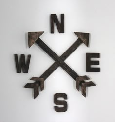 a metal clock with arrows and the word w e s written in black on a white wall