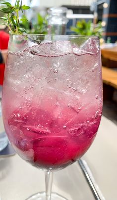 a glass filled with ice and water on top of a table next to a plant