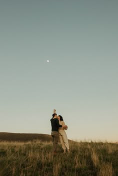 two people standing in a field under a clear blue sky with the moon behind them