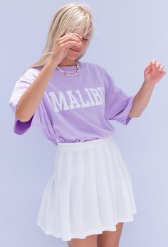 The Malibu Days Tee with oversized fit, short sleeve and Malibu front graphic. Worn with the Paris In A Day Pleated Mini in White. Color: Lilac Short Sleeve Oversized Fit Cotton Model is 5'7", 32A Bust & Wearing Size Small/Medium Oversized Purple T-shirt For Summer, Oversized Purple T-shirt With Letter Print, Summer Purple T-shirt With Logo Print, Summer Purple Logo Print T-shirt, Oversized Purple Top With Text Print, Oversized Short Sleeve Shirt With Logo Print, Oversized Purple Screen Print Top, College Short Sleeve Shirt With Logo Print, Casual Short Sleeve Shirt With Logo Print