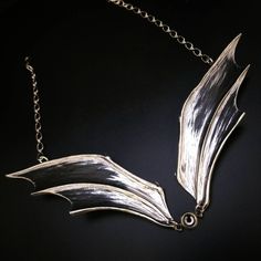 a silver necklace on a black surface with a chain hanging from the neck and a leaf shaped pendant attached to it