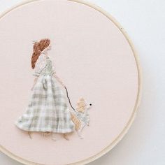 a woman in a dress is holding a small dog on a pink background with a cross stitch hoop