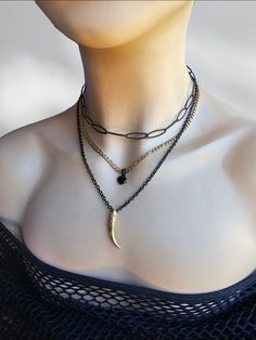 A black steel and 24 K gold filled steel Gothic Grunge alt aesthetic choker chain layered necklace set with heart and tusk pendants. The set is two separate necklaces that can be worn together or separate, one is a black steel horse eye paperclip chain choker with a built-in extender that runs from approximately 14" to 16". it also features a two strand necklace, one black steel with a gold filled tusk pendants and the other 24 K gold filled steel chain with a black heart charm. It is an adjustable length from approximately 16" to 18" with a built-in extender.  This necklace set is an excellent handmade gift for someone special. It is a perfect choice for those who love alternative and goth styles, as well as anyone who wants to make a statement with their jewelry. Black Grunge Necklace For Gift, Trendy Black Jewelry With Double Chain, Trendy Black Double Chain Jewelry, Black Grunge Necklace With Adjustable Chain, Edgy Black Chain Necklace For Gifts, Edgy Gold Necklace For Gifts, Edgy Gold Necklace For Gift, Trendy Black Layered Necklace As A Gift, Trendy Black Layered Necklace For Gift