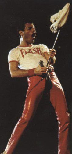 a man in red pants and white shirt holding a stick with his right leg up