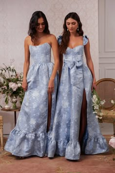 two women standing next to each other in blue dresses with flowers on them and one wearing a high slit skirt