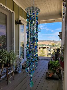 a blue glass wind chime hanging from the side of a porch next to potted plants