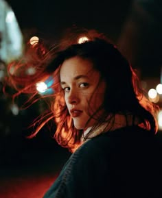 a woman with her hair blowing in the wind on a city street at night time