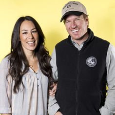 a man and woman standing next to each other in front of a yellow wall smiling