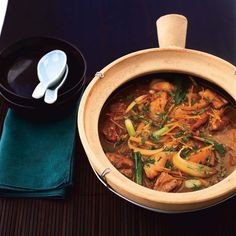 a wooden bowl filled with meat and vegetables next to a spoon on top of a table