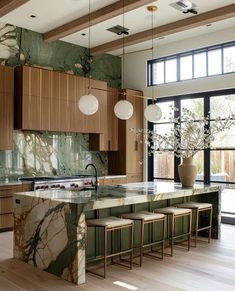 a large kitchen with marble counter tops and wooden cabinets, along with four stools