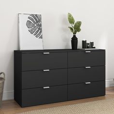 a black dresser with two plants on top of it next to a white wall and wooden floor