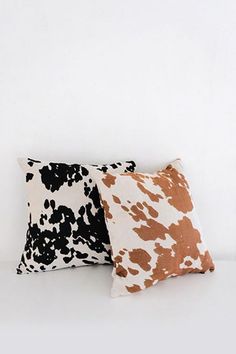 two black and brown pillows sitting next to each other on a white surface, one with an animal print pattern