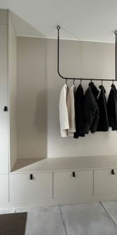 an open closet with clothes hanging on the hooks and two white cabinets in front of it