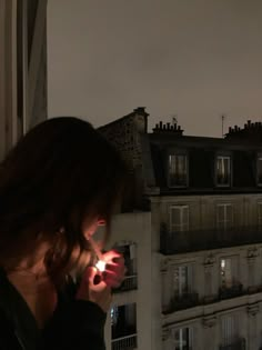 a woman looking at her cell phone while standing in front of a window with the city lights on