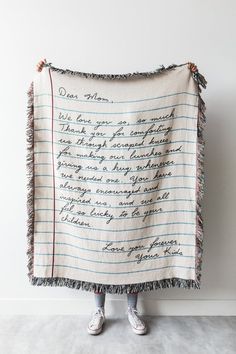 a person standing in front of a wall holding a white blanket with writing on it