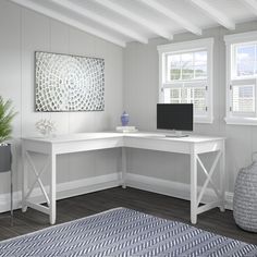 a white desk sitting in the corner of a room next to two windows and a rug