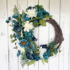 a wreath with blue flowers and greenery on a white wooden background, hanging from the wall