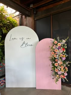 a pink and white arch with flowers on it next to a sign that says love is an born