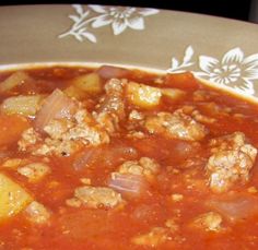 a bowl of soup with meat and potatoes on a tableclothed place mat, ready to be eaten