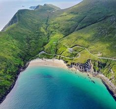 an aerial view of the ocean and coastline with green hills in the background, along with blue water