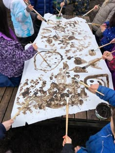 children doing arts and crafts with sticks on a white table cloth covered in brown dirt