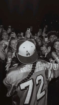 a man in a baseball cap is surrounded by fans and taking pictures with his cell phone