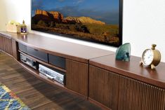 a flat screen tv sitting on top of a wooden entertainment center next to a wall mounted clock