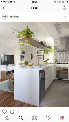 a kitchen with white walls and wooden floors has an island in the middle that is surrounded by hanging plants