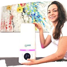 a woman is holding an alarm clock in front of her face and painting on the wall behind her