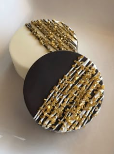 a cake with gold and black icing on it sitting on a white table next to a cupcake