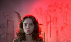 a woman standing in front of a wall with graffiti on it and red light coming from behind her