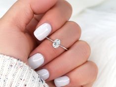 a woman's hand holding a ring with a diamond on it and a white sweater