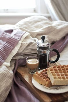 waffles and coffee are sitting on a tray with a blanket in the background