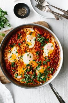 an egg dish in a skillet with parsley on the side and two spoons next to it