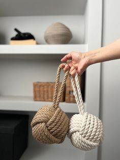 a hand holding two rope balls in front of a book shelf filled with books and other items