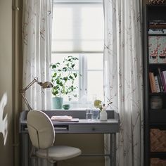 a desk with a chair, plant and bookshelf in front of the window