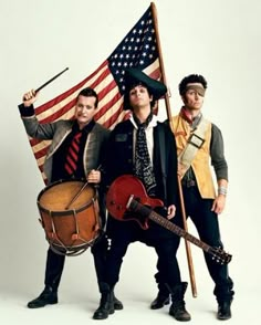 three men are holding flags and drums while posing for a photo in front of an american flag