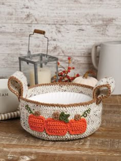 a crocheted basket with pumpkins and leaves on the inside, sitting on a wooden table