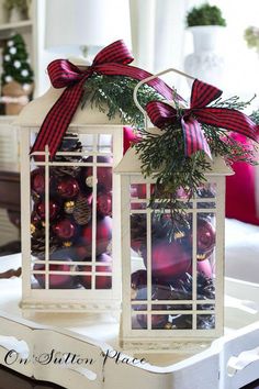 two white lanterns decorated with red and green christmas ornaments on a tray in front of a window